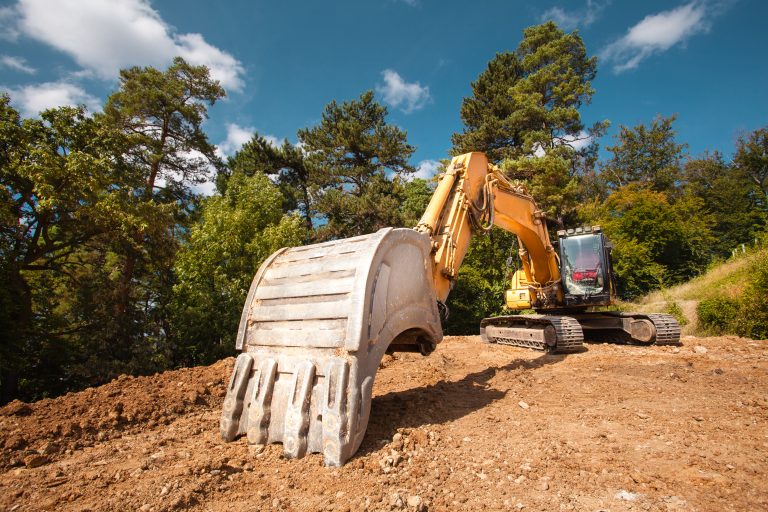 perspective view of excavator on new construction site with trees and blue sky in background