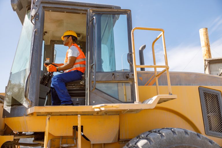 Skillful factory worker in protective uniform, using heavy-duty vehicle at construction industry plant