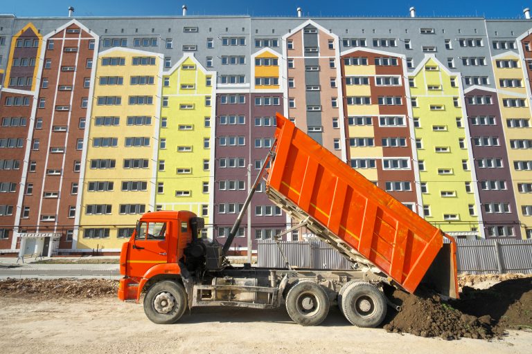 Building urban scene. Multistorey building apartment house and dump truck unload soil at day.